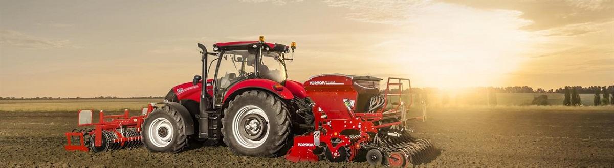 A red tractor tilling a dirt field during sunset